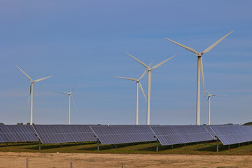 Solar panels and wind turbines under blue sky. Green energy concept.