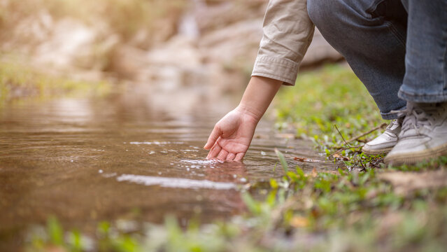 Close-up hand image of a woman touching the water in a small nature canal waterfall on the mountain