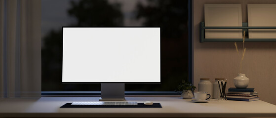 Front view of a white-screen computer mockup on a table in a modern home office at night.