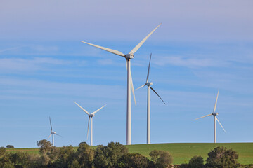Fototapeta premium Wind turbines with landscape of agricultural fields under blue sky. Green energy concept.