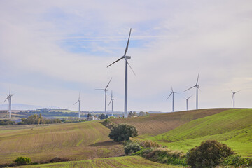 Obraz premium Wind turbines with landscape of agricultural fields under blue sky. Green energy concept.