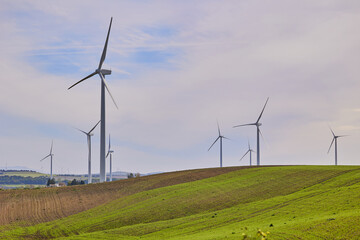 Obraz premium Wind turbines with landscape of agricultural fields under blue sky. Green energy concept.