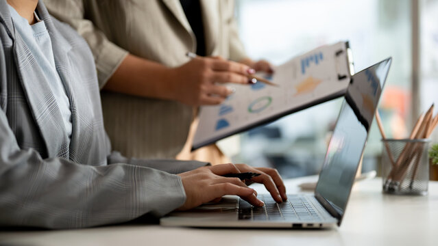 A businesswoman working on her laptop computer and discussing work with her colleague in the office.