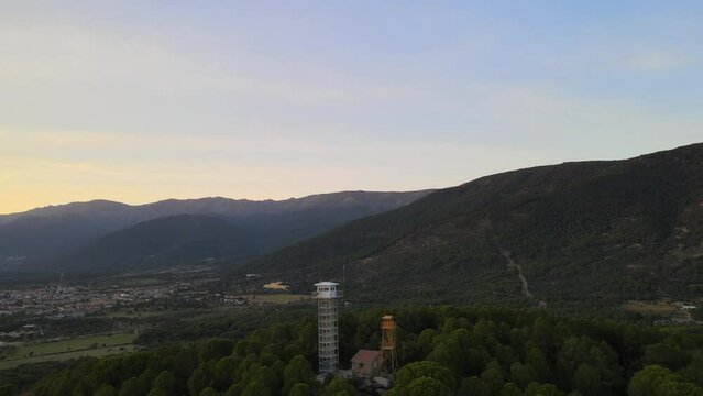 reverse flight with dro visualizing a fire surveillance post located at the top of a hill and a town, with mountains in the background