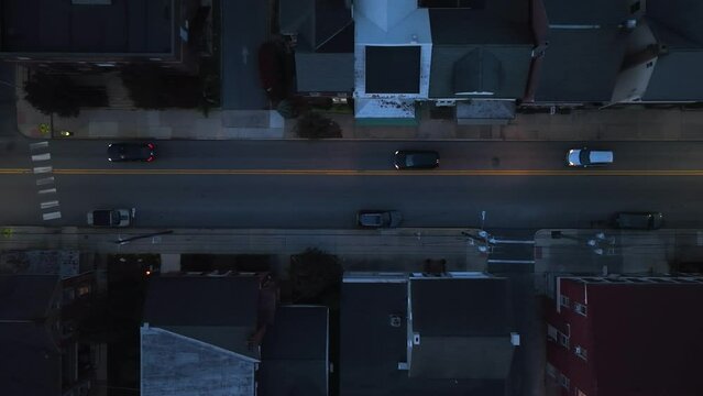 Top down aerial of traffic in small town USA at night. Tracking shot of cars on American road lined by town homes.
