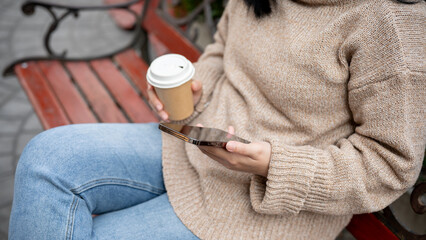 A woman relaxing at a table in a garden or a cafe outdoors seat, sipping coffee and using her phone.