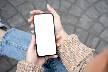 A woman in casual clothes is relaxing on a bench in a city park and using her smartphone.