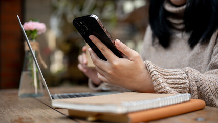 An Asian woman using her smartphone, responding to messages while sitting at a table in a cafe.