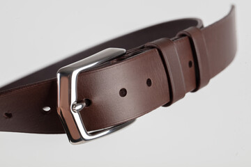 Part of a brown leather classic belt with a buckle on a gray background.