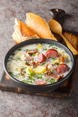 Zalewajka is a traditional Polish soup made from whole wheat soup starter, smoked sausage, aromatic smoked bacon and root vegetables closeup on the plate on the table. Vertical