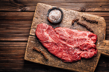 Raw Chuck eye beef steak seasoned with salt and pepper on wooden cutting board