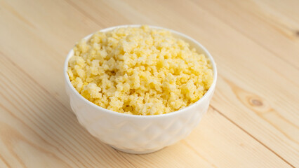 Millet porridge in white cup on wooden background, selective focus