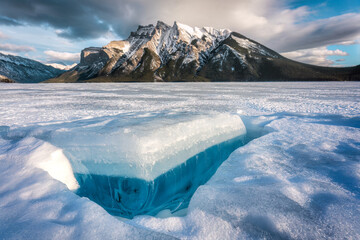 Frozen Lake Minnewanka with rocky mountains and cracked ice from the lake in winter at Banff...