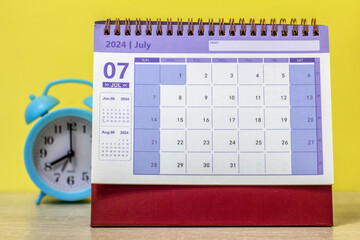 Desk calendar for July 2024 on the table next to the alarm clock. - obrazy, fototapety, plakaty