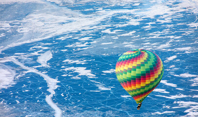 Hot air balloon flying over Ogoy island on winter Baikal lake with transparent cracked blue ice at...