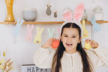 Happy easter! A beautiful child girl wearing bunny ears painting colorful eggs and have fun