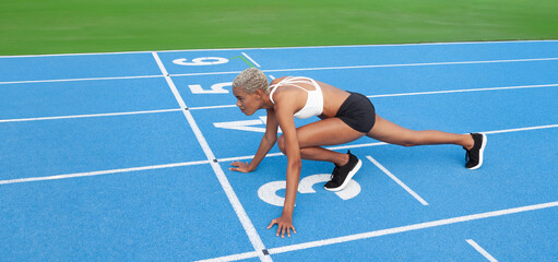 An African American female athlete stands poised at the starting line on the Olympic blue track,...
