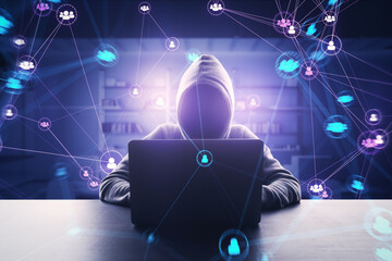 Hacker in hoodie using laptop at desk with connected digital people team icons on dark blurry...