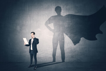 Attractive young european businessman with document and phone standing on concrete wall background...