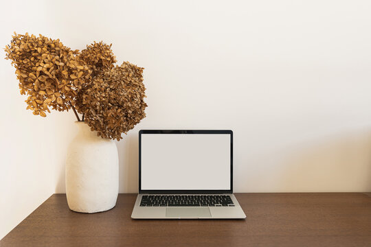 Laptop computer with blank screen. Dried hydrangea flower bouquet on wooden table. Minimal online shop, store, social media template with mockup copy space