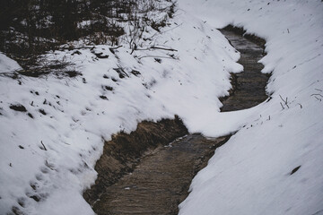 Fresh clean drainage ditch covered with snow in winter forest. Water running at bottom