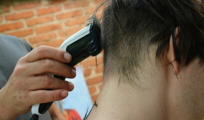 a man's hand holds a hair clipper with a nozzle and cuts the back of a young man's head, close-up,...
