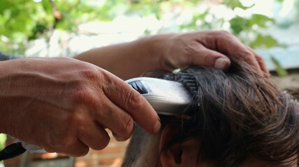 hands of a hairdresser cutting the back of a person's head with a clipper, close-up, shaving long...