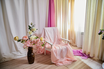 Delicate bright pink interior of the room with armchair, a vase with roses, draped curtains and a...