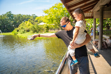 Father and daughter feeding many gigantic asian catfishes in zoo of Thailand