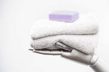 Robot arm holding terrycloth towels and a bar of soap. The image symbolizes the care of people by machines. Conceptual photo against a white background with text space.