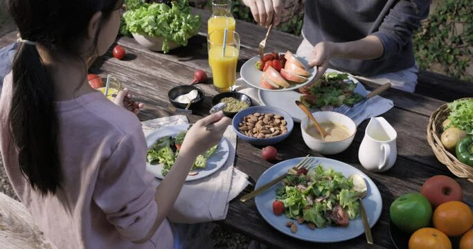 Father mother and daughter eating fresh vegetable salad with fresh vegetables, tomatoes, bell pepper, potato, fruits and dipping sauces on wooden desk at outdoor garden, Conceptual of party family hea