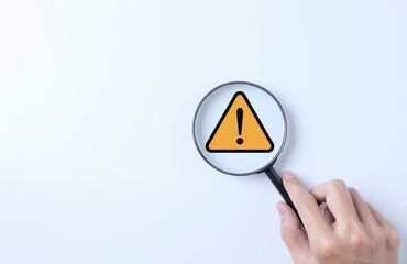 Warning alert system concept. Magnifying glass focused on yellow triangle warning sign....
