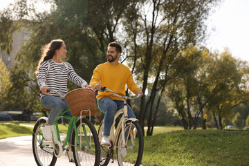 Beautiful couple riding bicycles in park, space for text