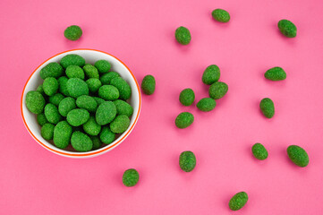 Bowl of peanuts in wasabi glaze a scattering of nuts on a fuchsia background.