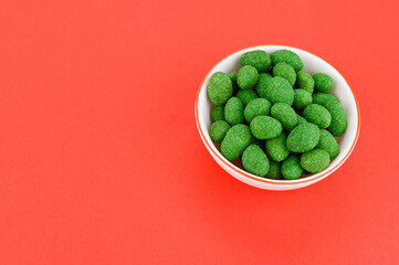 Bowl of peanuts in wasabi glaze on a red background. Place for the text.