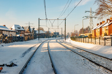 Front view of snow covered train tracks between houses and buildings, blurred misty background,...