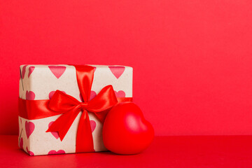 gift box with red bow and red heart on colored background. Perspective view. Flat lay