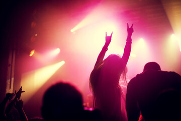 Rock, concert and people dance at night, event or party at music festival with fans in audience at stage. Crowd, energy and woman with hands in sign for metal, sound or social celebration at rave