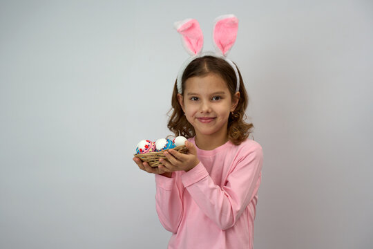Girl wearing pink bunny ears and shirt and holding basket with colorful Easter eggs