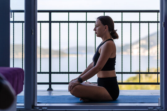 Yogi woman in sportswear meditating sitting on the mat at the balcony
