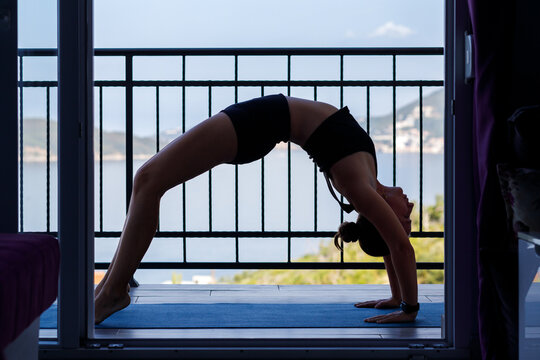 Yogi woman in sportswear performing wheel yoga pose at the balcony