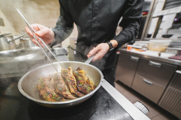 man chef cooking fried meat slice in frying pan on restaurant kitchen
