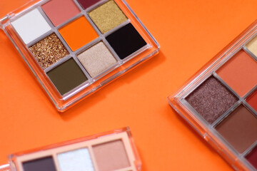Colorful eyeshadow palettes and make up brush on orange background. Selective focus.