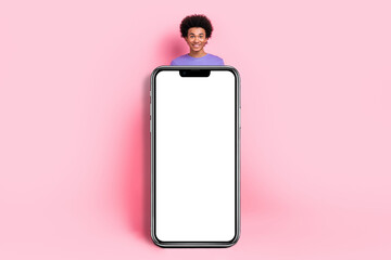 Full size photo of cheerful guy wear t-shirt pants hands hold big smartphone touchscreen empty space isolated on pink color background