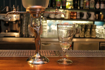 Absinth fountain and glass with spoon on bar counter close-up.