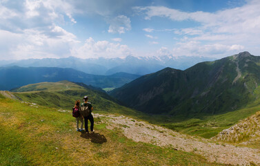 Couple woman and man wearing wide sun hat and backpack, tourists on hiking trail to Koruldi Lakes, Svaneti region, Mestia Georgia. travel and active recreation. Summer day. Aerial. Copy space