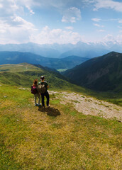 Fototapeta na wymiar Couple woman and man wearing wide sun hat and backpack, tourists on trail to Koruldi Lakes, Mestia Georgia. The concept of travel and active recreation. Summer day. Aerial vertical photo
