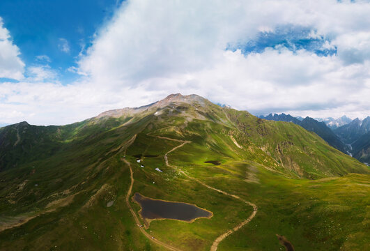 Aerial view at the Koruldi lakes. Green hills, high mountain pastures. Summer day. in the background are the snowy peaks of the Caucasus Mountains. High resolution panorama. Ushba, Georgia