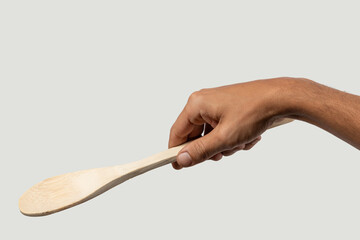 Black male hand holding a wooden cooking spoon on grey background.