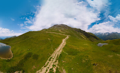 Aerial view at the Koruldi lakes. Green hills, high mountain pastures. Summer day. in the background are the snowy peaks of the Caucasus Mountains. High resolution panorama. road, trail to Ushba